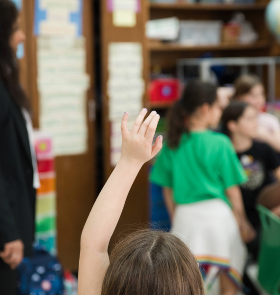 Young student raising her hand with her classmates in the background